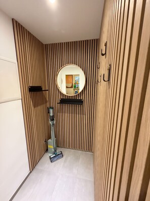 A bathroom with a wooden slat wall, a round mirror, a handheld vacuum cleaner, and a shelf with toiletries.