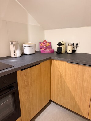 A kitchen with a countertop, a coffee maker, a rice cooker, a box of tea, and a kettle.