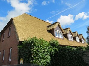Ein traditionelles Haus mit Strohdach, Backsteinwänden und einer mit Efeu bewachsenen Fassade.