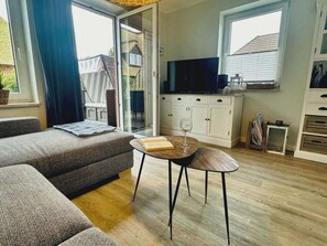 Ein modernes Wohnzimmer mit einer Couch, einem Couchtisch, einem Fernseher und einer Schiebeglastür zu einem Außenbereich.