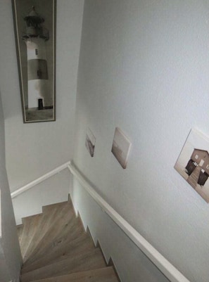 Eine Treppe mit Holzsitzstufen und weißen Sockelleisten, die zu einem Zwischenpodest mit einer hellgrauen Wand führt.
