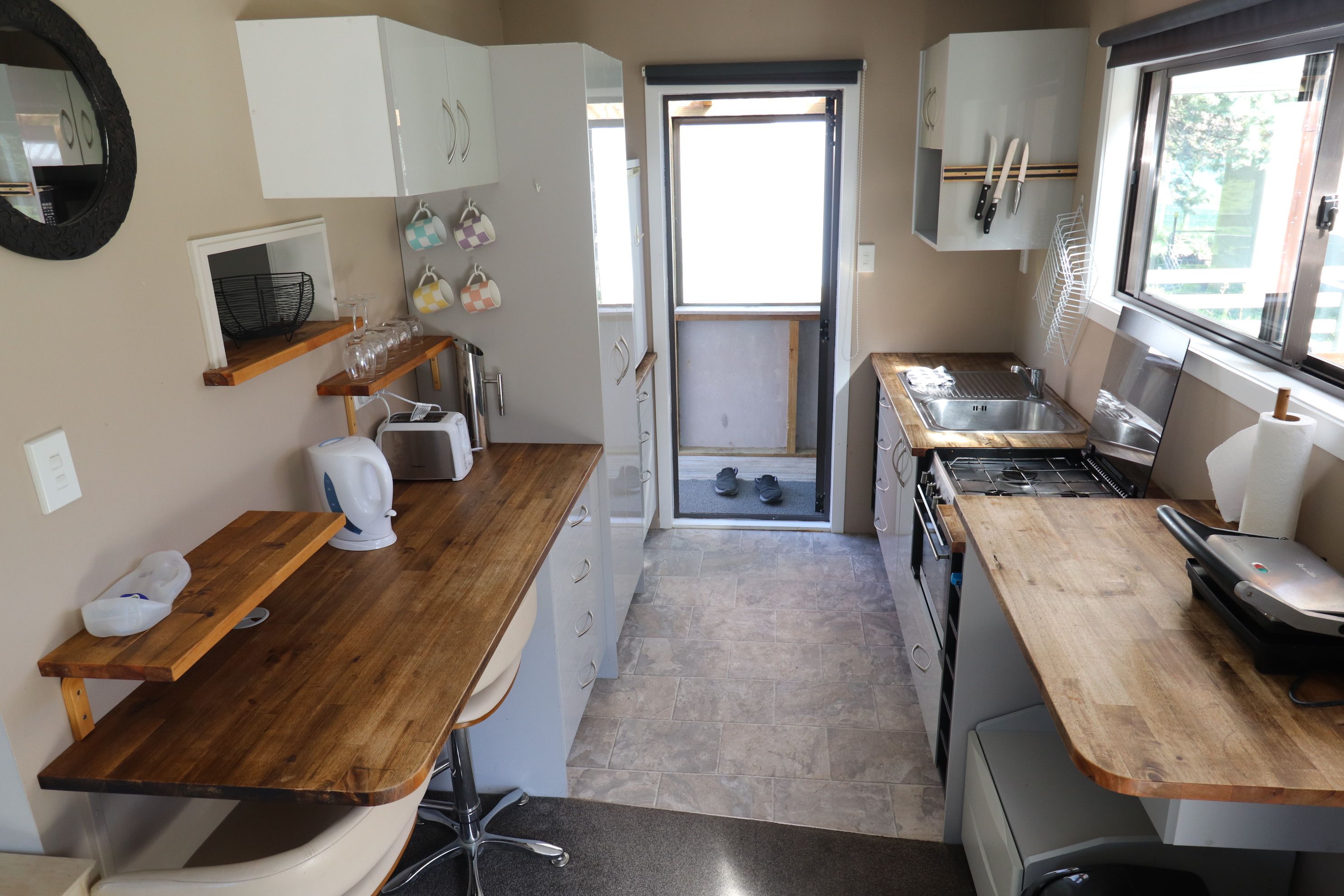 Une cuisine compacte dotée de plans de travail en bois, d’un four encastré et d’une fenêtre laissant entrer la lumière naturelle.