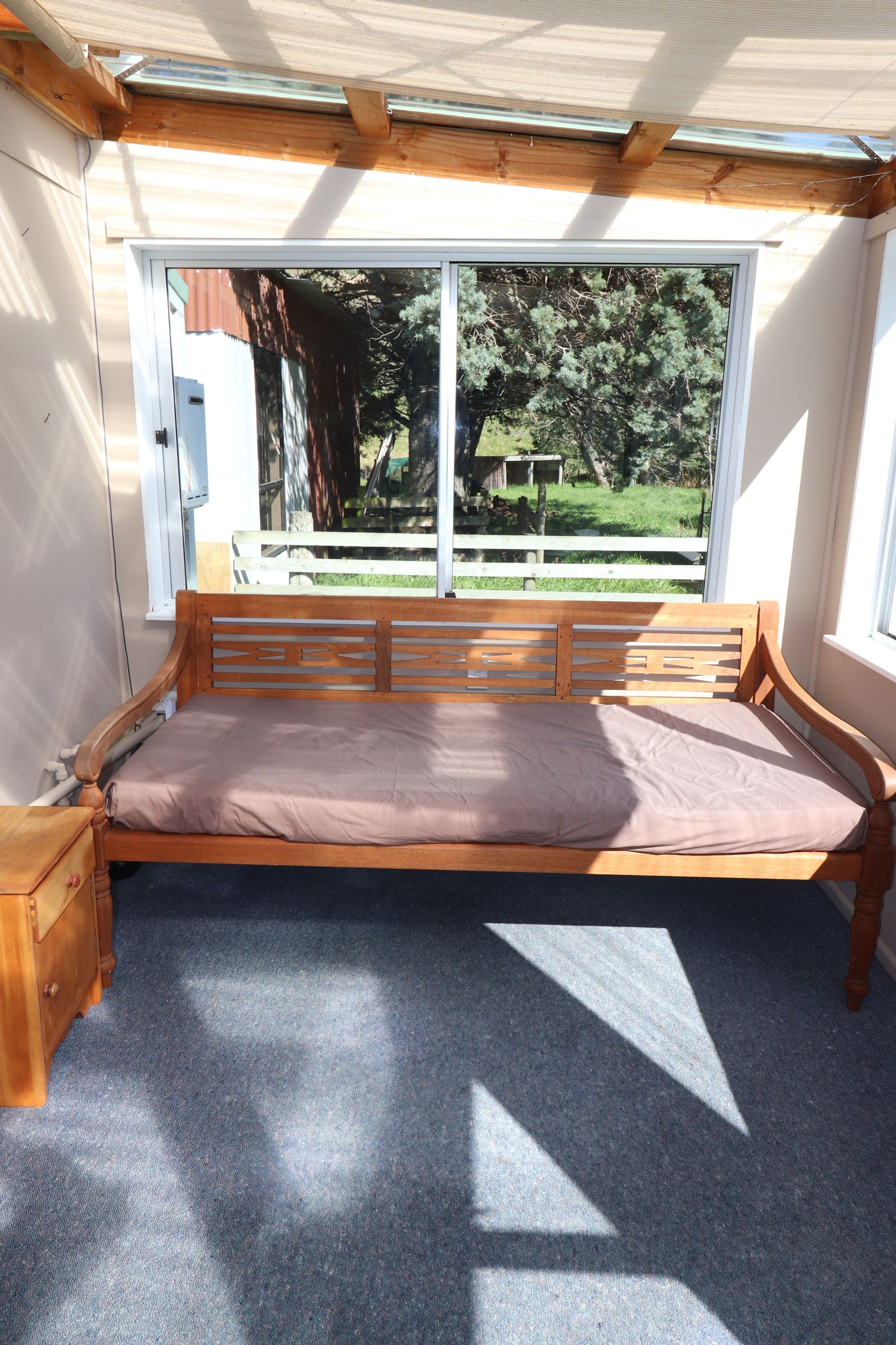 Ein Zimmer mit einer hölzernen Bank, einem Fenster und Blick ins Freie.