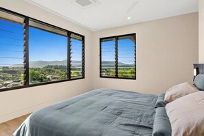 Ein Schlafzimmer mit einem großen Bett, zwei Fenstern mit schwarzen Rahmen und Blick auf eine Berglandschaft.