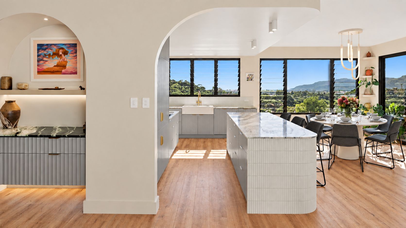A modern kitchen with a central island, large windows, and a dining area with a view.