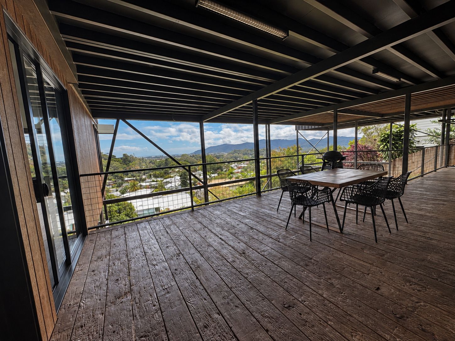 An outdoor patio with a wooden deck, metal railing, and a table with chairs.