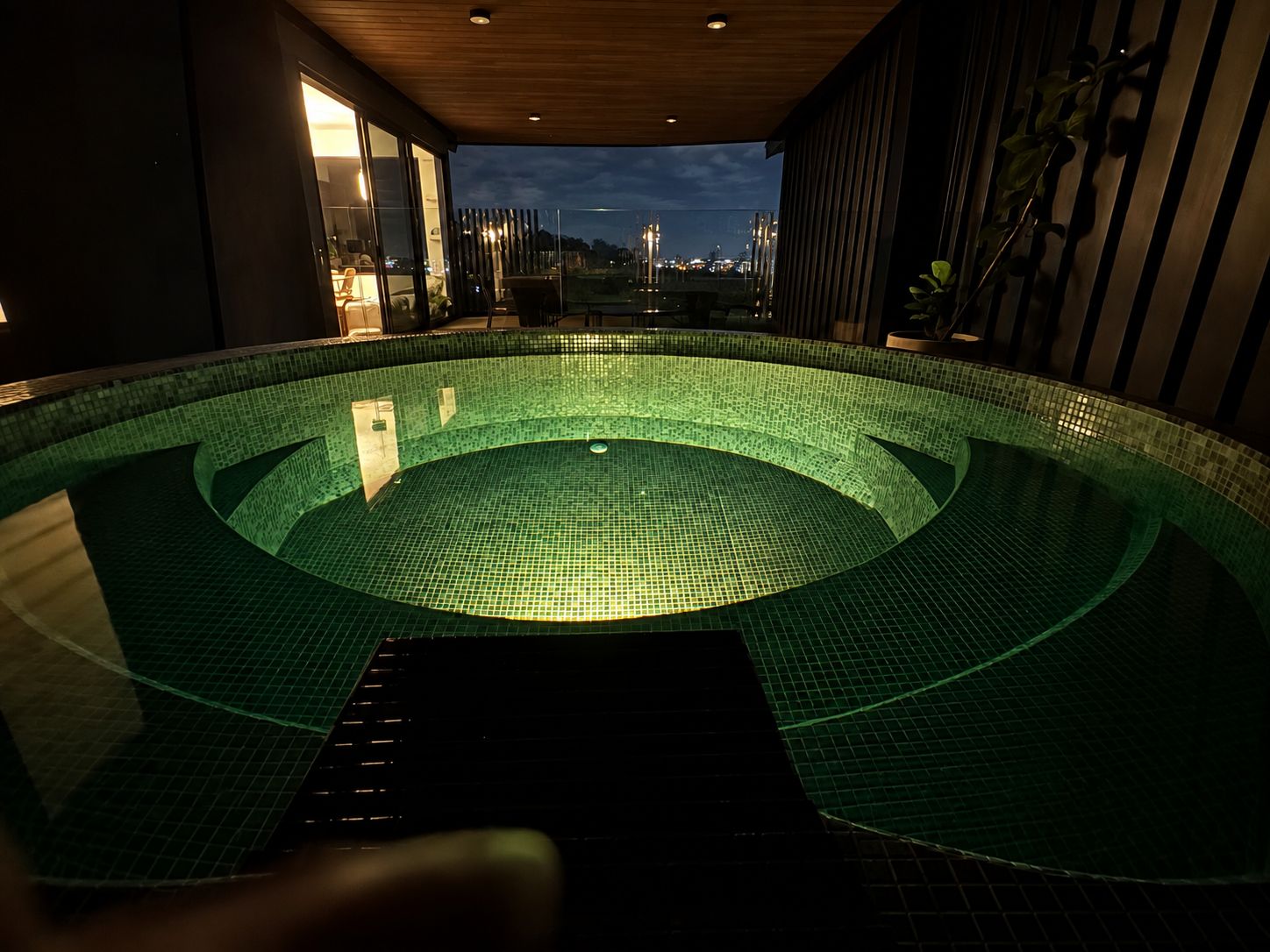 An indoor swimming pool with a tiled interior and a view of the cityscape at dusk.