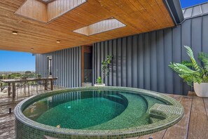Ein moderner Poolbereich im Freien mit Holzterrasse, einer Sitzecke und Blick auf die Stadt.