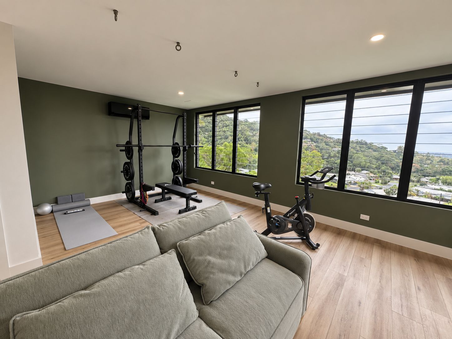 A spacious room with a large window, a weightlifting station, an exercise bike, and a sofa.