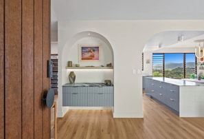 Una cocina moderna con una isla central, suelo de madera y vistas a un paisaje a través de amplios ventanales.