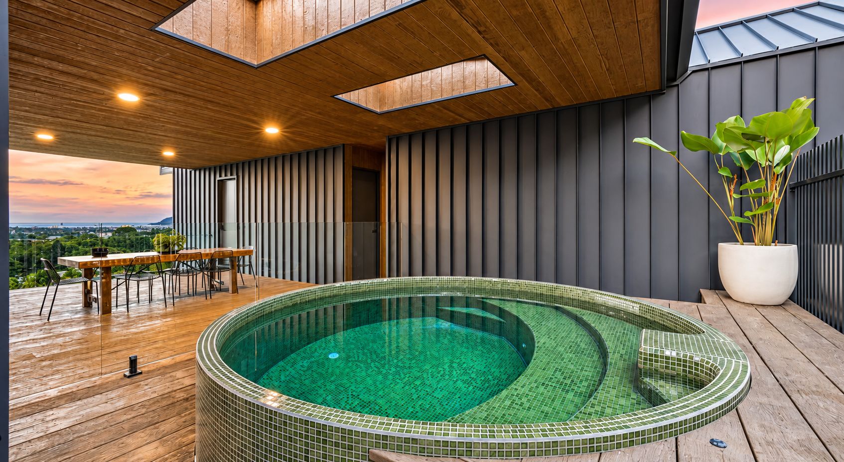 Een modern zwembadgedeelte buiten, met een houten terras, een jacuzzi en een eettafel met stoelen.
