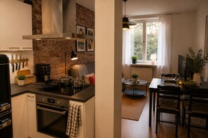 A modern kitchen with a brick wall, stainless steel appliances, and a dining area with a table set for two. - Modern Scandinavian Apartment in Central Helsinki (Helsinki)