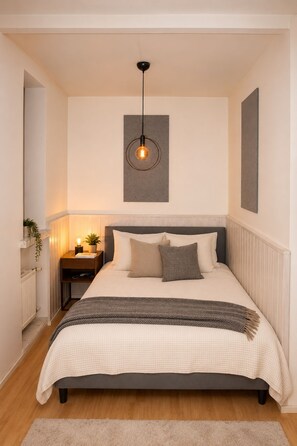 A bedroom with a bed, bedside tables, a hanging light fixture, and a radiator. - Modern Scandinavian Apartment in Central Helsinki (Helsinki)