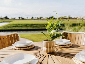 Ein runder Holztisch mit weißen Tellern und einer beigen Vase mit grünen Blättern.