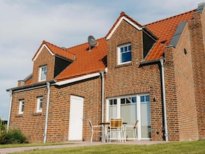 Ein zweistöckiges Backsteinhaus mit rotem Ziegeldach, einer Satellitenschüssel und einer kleinen Terrasse mit Gartenmöbeln.