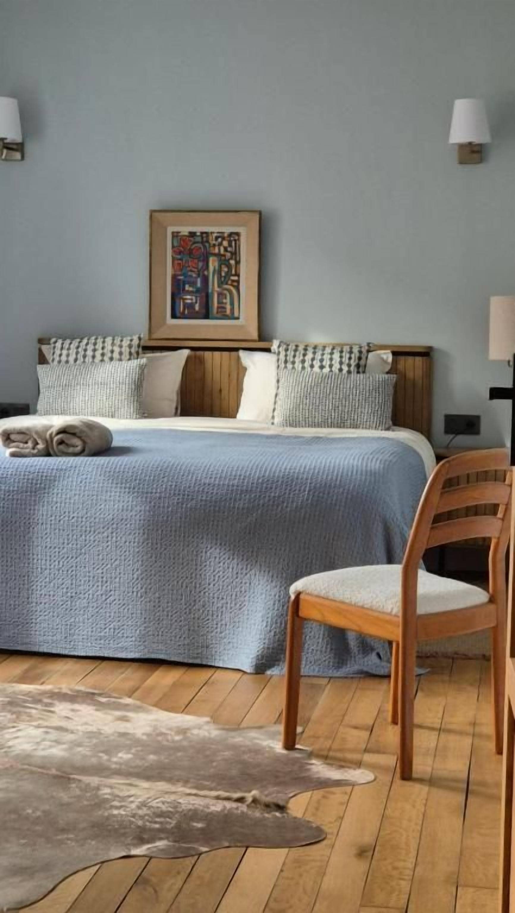 Un dormitorio con cama, almohadas, una silla, una alfombra y un cuadro colgado en la pared.