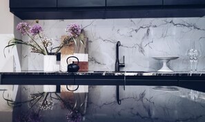 Una cocina moderna con encimera de mármol, grifo negro, un florero blanco con flores y tabla de cortar de madera.