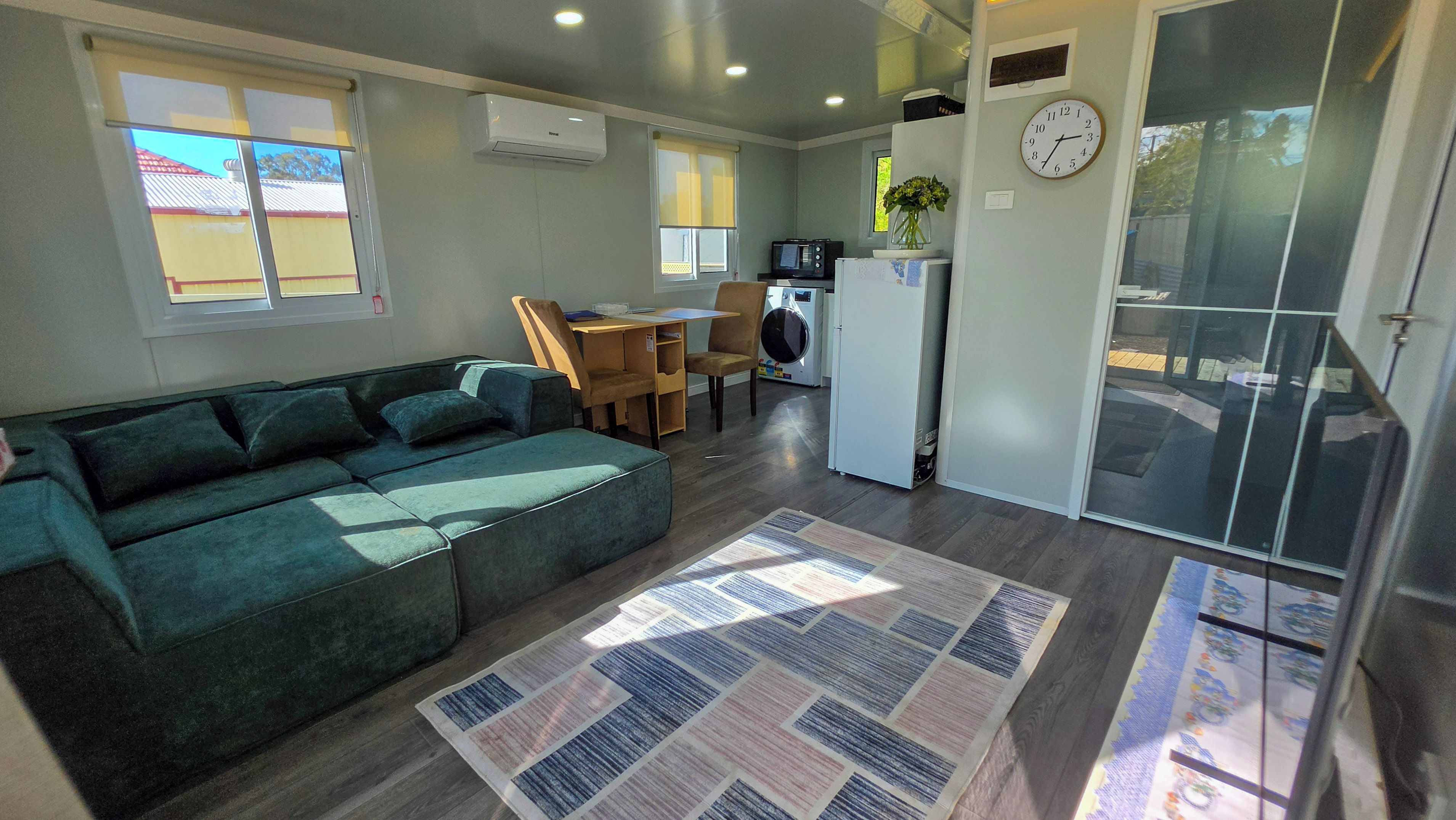 A compact living space with a sofa, a dining table with chairs, a small kitchen area, and a sliding glass door.