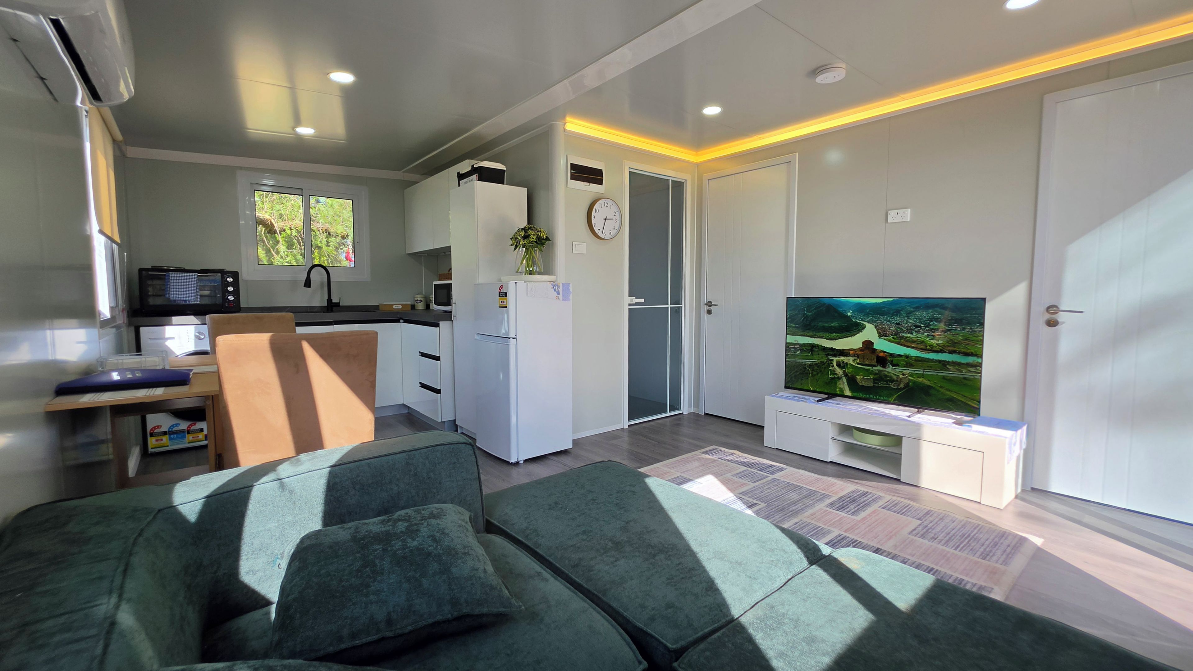 A modern living room with a sofa, a flat-screen TV, and a kitchen area with a microwave and refrigerator.
