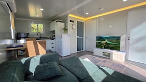 Ein modernes Wohnzimmer mit einer Couch, einem Flachbildfernseher und einer Küchenzeile inklusive Mikrowelle und Kühlschrank.