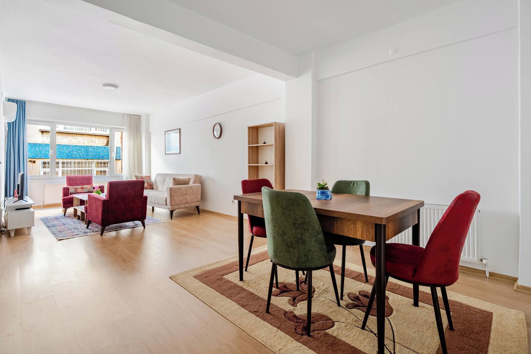 A modern living room with a dining area, a sofa set, a coffee table, a bookshelf, and a view of the outside.