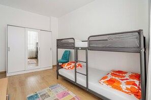 Ein Zimmer mit Etagenbetten, einem Kleiderschrank, einem türkisfarbenen Sessel und einem bunten Teppich.