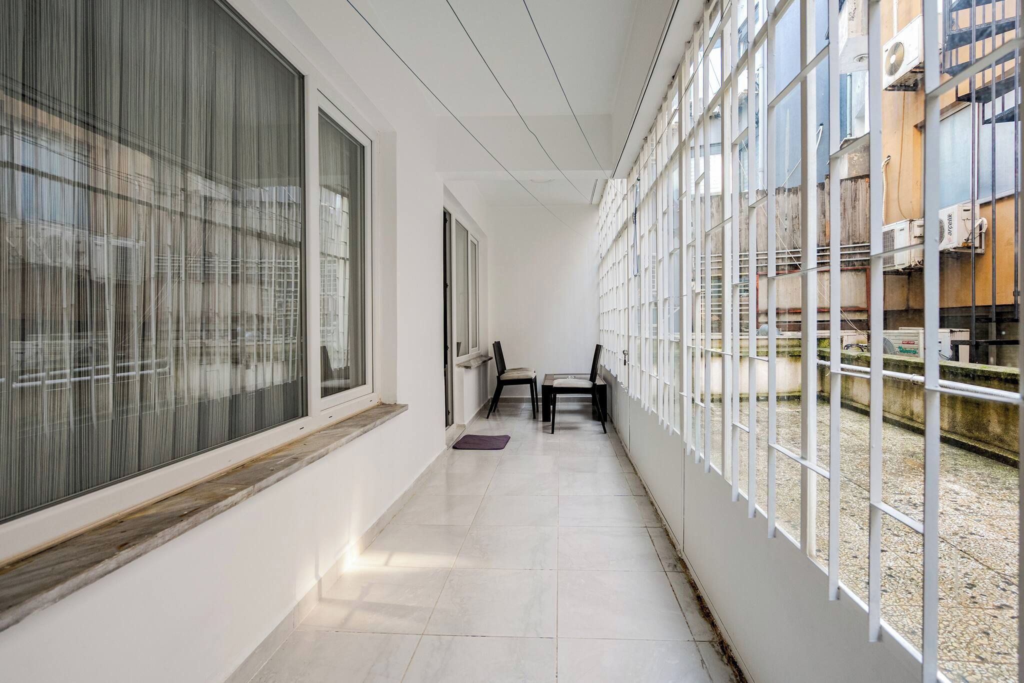 A corridor with a table and chairs, large windows, and a view of the outside.