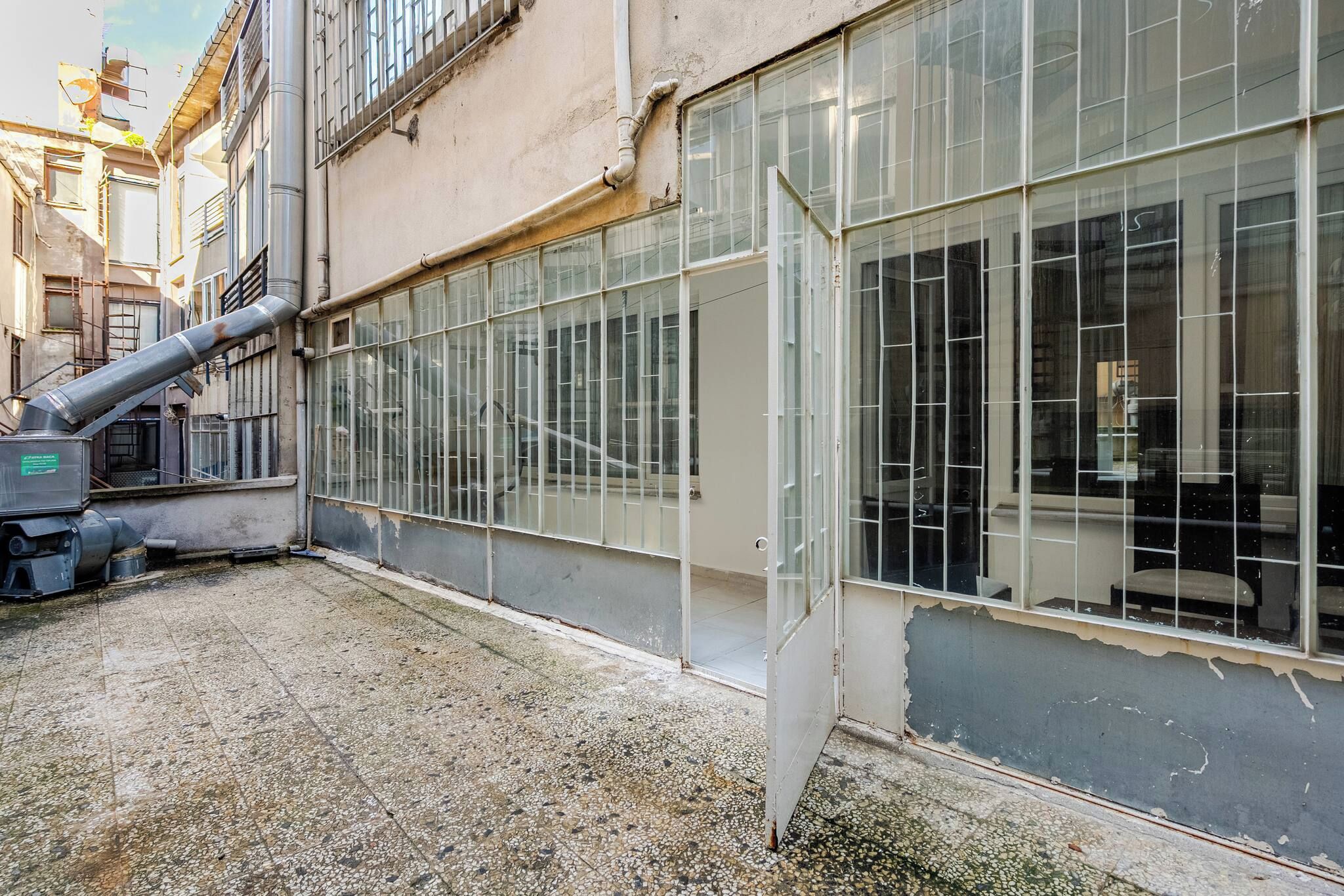 A building with large windows, a visible pipe, and a gravel ground.