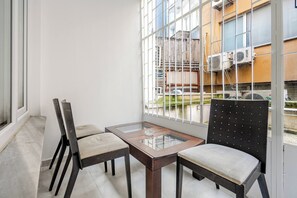 A balcony with a glass table and two chairs, overlooking a building with air conditioning units. - Cozy Central Apartment in the Heart of Kadıkoy (Istanbul)