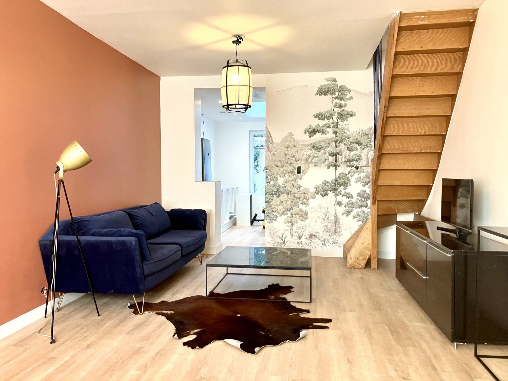 Een moderne woonkamer met een blauwe bank, een glazen salontafel, een leren vloerkleed, een staande lamp en een trap.
