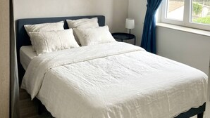 Een slaapkamer met een bed, een nachtkastje, een lamp, een raam met gordijnen en een hanglamp.