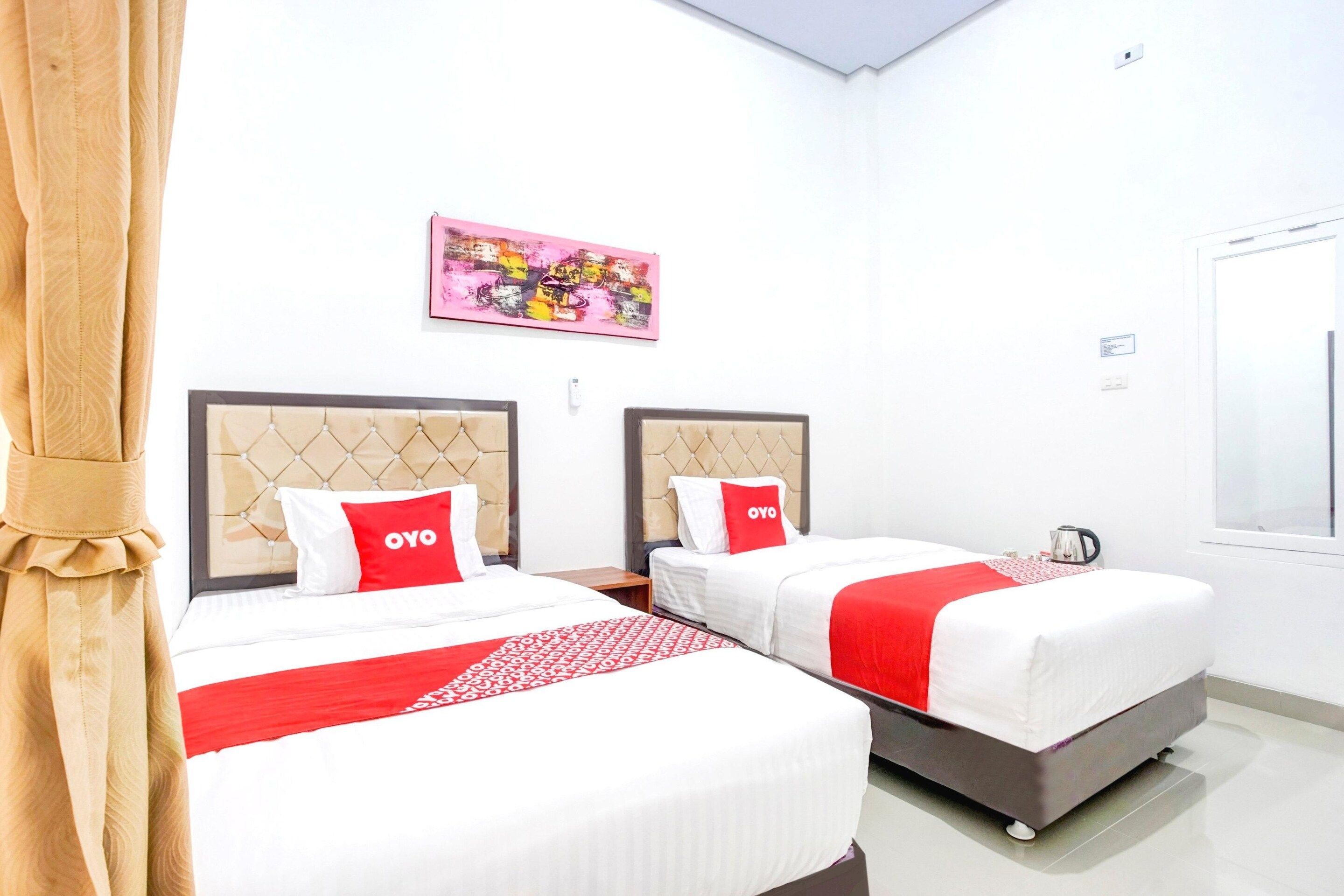 A hotel room with two beds, each with a headboard, a red and white bedspread, and a red pillow with 'OYO' branding.