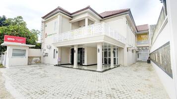 A two-story building with a balcony, a covered entrance, and a paved courtyard.