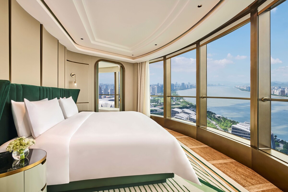 Habitación de hotel con una cama grande, vistas a un paisaje urbano y un balcón.