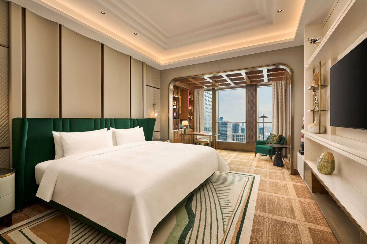 Habitación de hotel con una cama grande, televisión, escritorio y vistas a la ciudad.