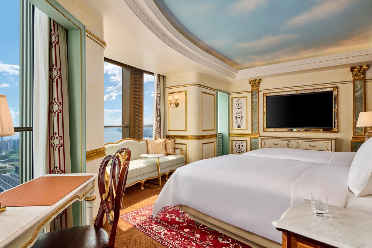 Habitación de hotel con una cama grande, un escritorio, una silla, un televisor y vistas a la ciudad.