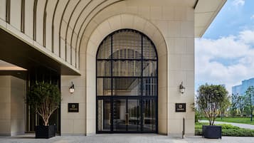 A hotel entrance with a large arched doorway, two potted plants, and a paved walkway.