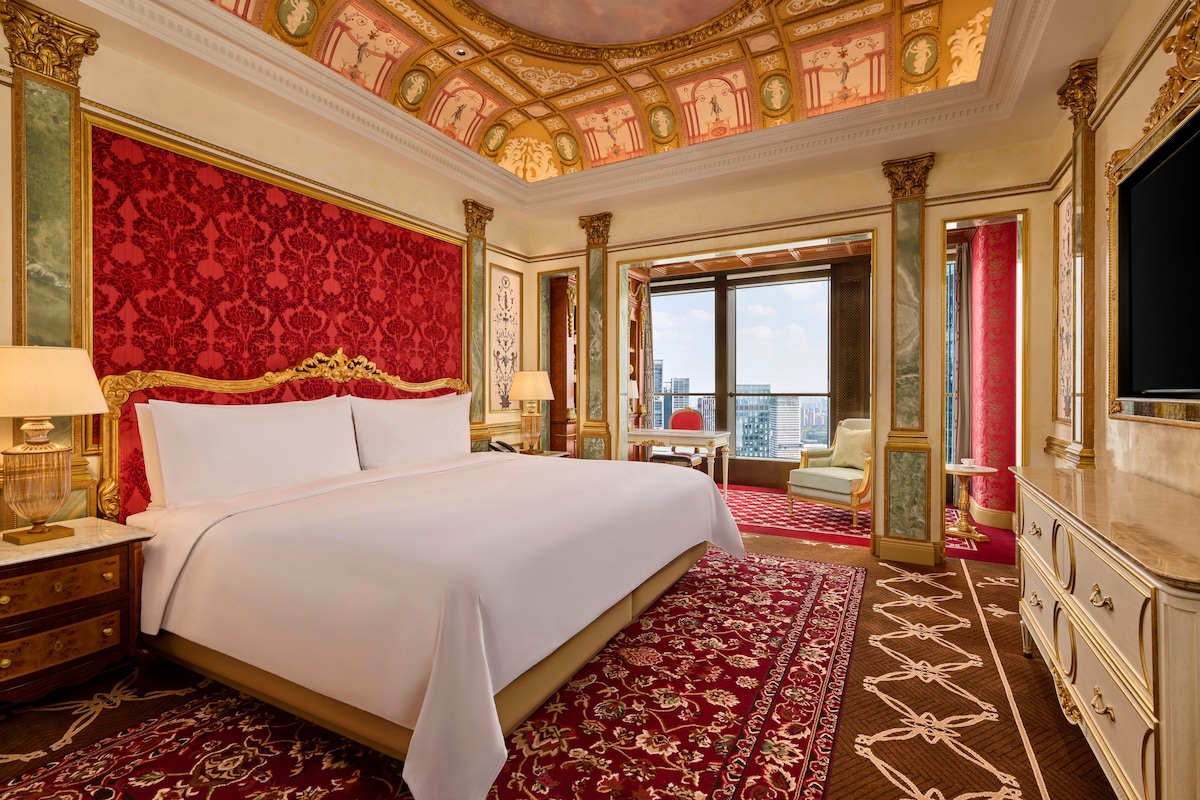 Una lujosa habitación de hotel con una cama grande, un techo ornamentado y vistas a la ciudad.