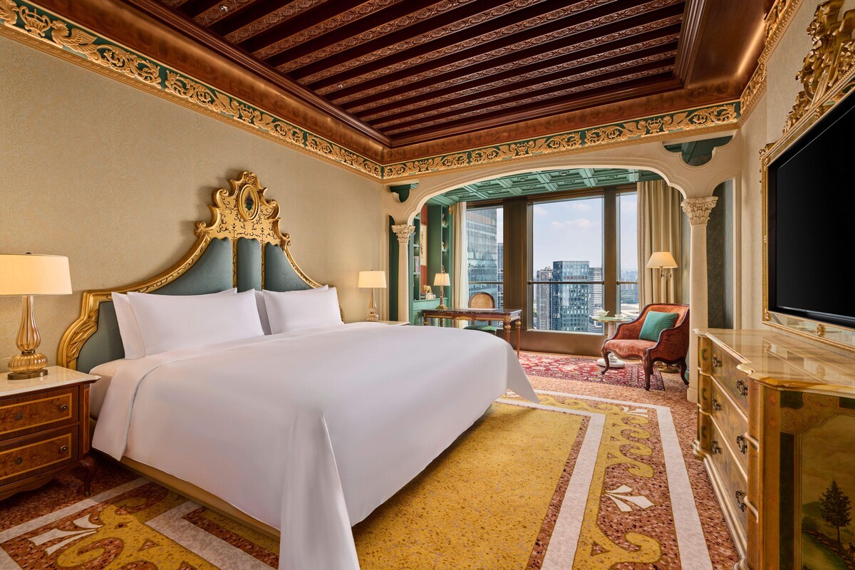 Una habitación de hotel con una cama grande, televisión, escritorio con silla y vista a la ciudad a través del ventanal.