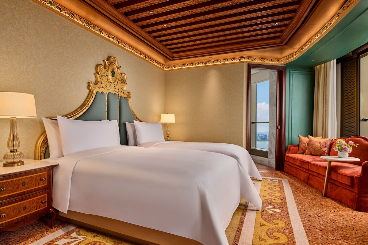 Habitación de hotel con una cama grande, zona de estar con sofá y vistas a la ciudad.