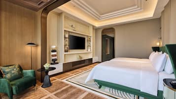 A hotel room with a large bed, a TV mounted on the wall, a small table with a vase, and a green armchair.