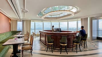 A high-rise hotel lobby with a central bar, seating area, and large windows offering city views.
