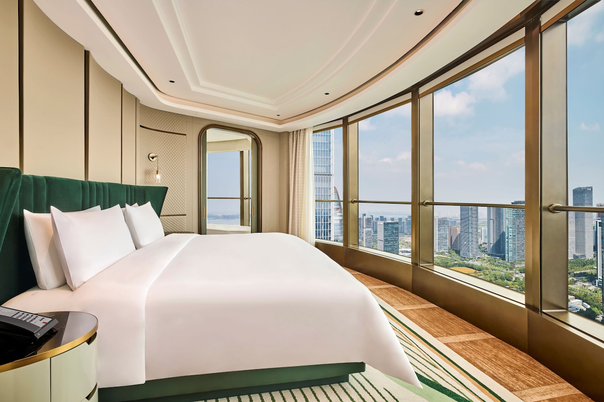 Habitación de hotel con una cama grande, vistas a la ciudad y un balcón.