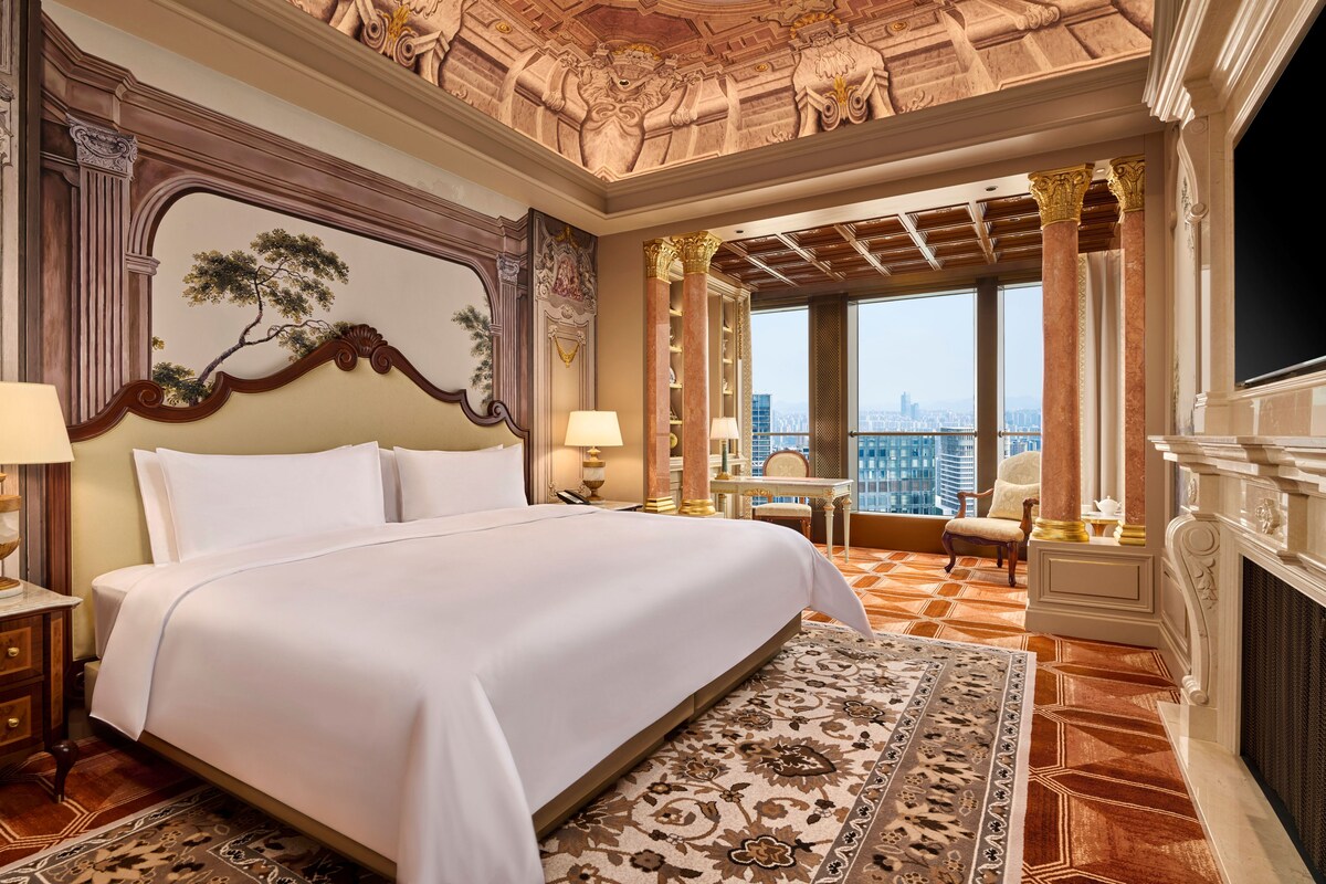Habitación de hotel con una cama grande, un escritorio, una silla y vistas a la ciudad desde la ventana.