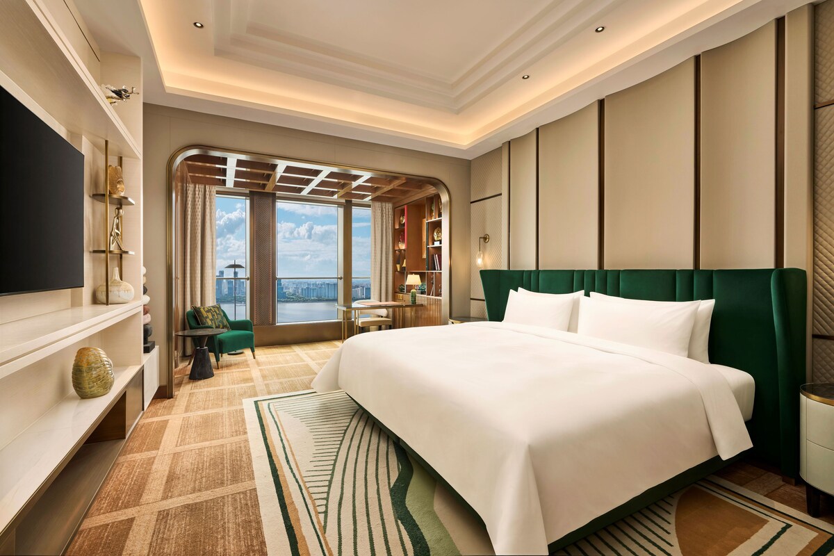 Una habitación de hotel con una cama grande, televisión, vista a la ciudad y un balcón con vista al río.