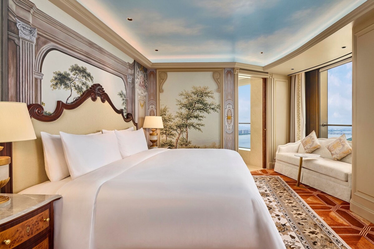 Habitación de hotel con una cama grande, un área de descanso y vistas, y un techo decorativo.