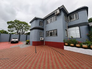 A two-story building with a red and grey exterior, a paved driveway, and a parked vehicle. - 95 on Queen Guest & Lodge – Peaceful Stay in a Great Location (Johannesburg)