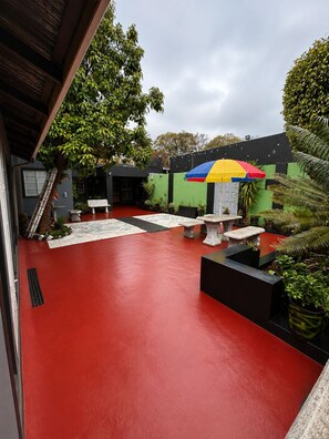 An outdoor patio area with a red floor, a colorful umbrella, and various seating arrangements. - 95 on Queen Guest & Lodge – Peaceful Stay in a Great Location (Johannesburg)