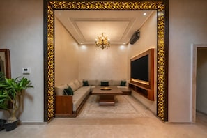 A modern living room with a sectional sofa, a coffee table, a flat-screen TV, and a decorative wall panel. - Villa Assi Prestige · 2 Private Hot Tubs, Breakfast & Airport Transfers (Marrakech)
