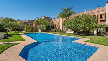 A rectangular swimming pool with a clear blue water surface, surrounded by a paved walkway, and adjacent to a building with a castle-like architectural style.